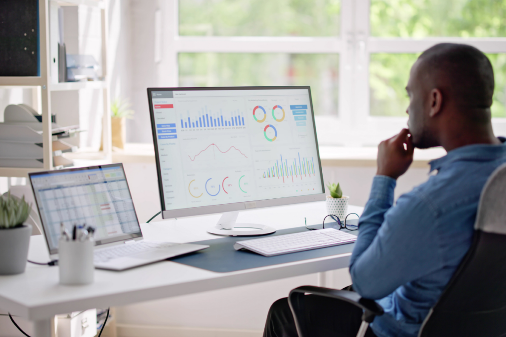 A man sitting at a desk, focused on a computer screen displaying data and analytics.