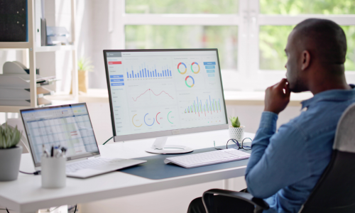 A man sitting at a desk, focused on a computer screen displaying data and analytics.