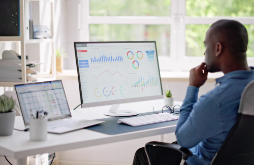 A man sitting at a desk, focused on a computer screen displaying data and analytics.